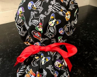 May include: Black scrub hat with a colourful Day of the Dead dog skull pattern. The hat has a red ribbon tied around it.