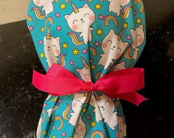 May include: A turquoise fabric pouch with a white unicorn cat print. The pouch is tied with a bright pink ribbon.