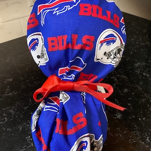 May include: A blue and red fabric scrub hat with the Buffalo Bills logo and the word "Bills" repeated on the fabric. The hat is tied with a red ribbon.