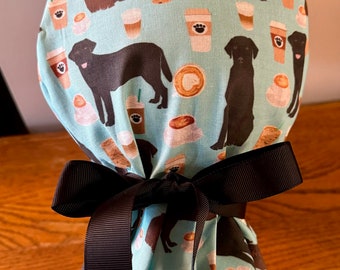 May include: A blue and white fabric scrub hat with a black ribbon tie. The fabric features a repeating pattern of brown labrador retrievers and coffee cups.