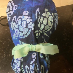 May include: A blue and white patterned surgical scrub hat with a light blue bow tied around it. The pattern features sea turtles.