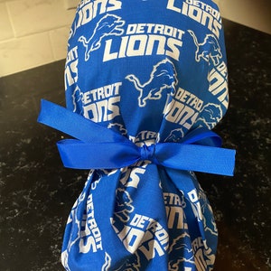 May include: A blue fabric gift bag with a white ribbon. The bag is decorated with a repeated pattern of the Detroit Lions logo.