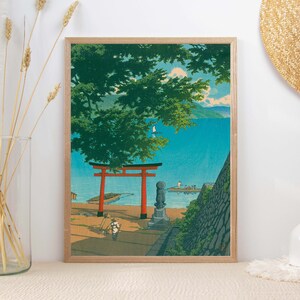 May include: A framed print of a Japanese landscape with a red torii gate, a green tree, and a blue body of water. The print is in a wooden frame.