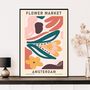 K&ouml;nnte beinhalten: Ein Poster mit dem Text "FLOWER MARKET AMSTERDAM" in schwarzen Buchstaben auf wei&szlig;em Hintergrund. Das Poster zeigt abstrakte Blumenformen in Rosa, Orange, Gelb, Gr&uuml;n und Braun.