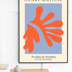May include: A framed print of a Matisse painting titled "Pavillon de Vend&ocirc;me Aix En Provence". The painting features a large, abstract orange shape on a blue background.