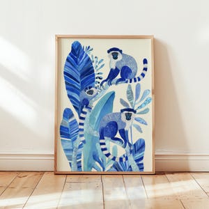 May include: Watercolor print of three blue monkeys perched on branches amidst blue foliage. The artwork is framed in a light wood frame, creating a nature-inspired aesthetic. The monkeys have white faces and striped tails.