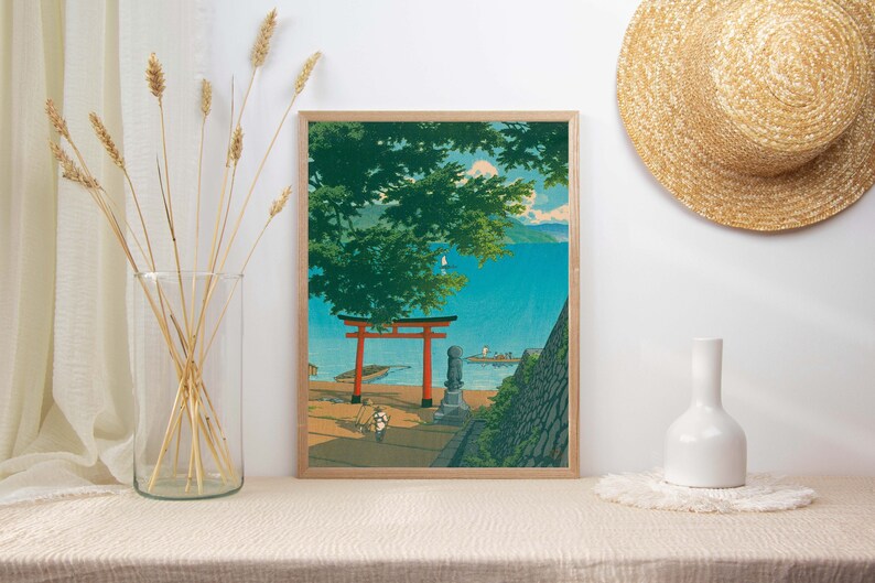May include: A framed print of a Japanese landscape with a red torii gate, a green tree, and a blue body of water. The print is in a wooden frame.