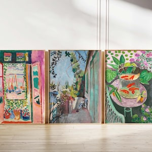Puede incluir: Tres impresiones artísticas enmarcadas con pinturas impresionistas coloridas. La obra de arte representa escenas de una ventana con vistas a un puerto, un balcón con plantas y un cuenco de peces dorados sobre una mesa. Los marcos son de color madera clara.