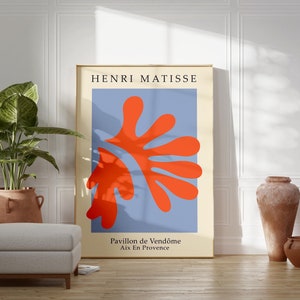 May include: A minimalist poster with a blue background and a large red abstract shape. The poster is framed in gold and has the text "HENRI MATISSE" at the top and "Pavillon de Vend&ocirc;me Aix En Provence" at the bottom.