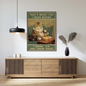 May include: A vintage-style poster featuring a cat sitting on a couch, reading a book and drinking tea. The text on the poster reads "That's what I do I read books I drink tea and I know things."