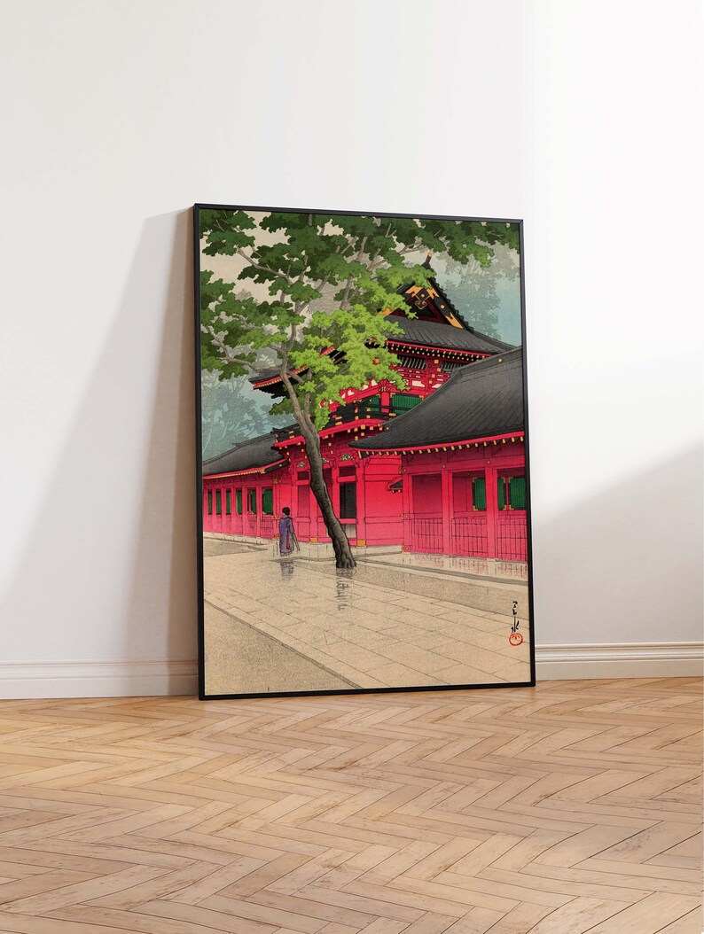 May include: A traditional Japanese woodblock print depicting a red temple with a green tree in the foreground. The temple has a black roof and white walls with red accents. The print is framed in black.