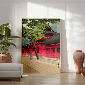 May include: A traditional Japanese woodblock print depicting a red temple with a green tree in the foreground. The temple has a black roof and is surrounded by a wooden fence. A person in a kimono is walking in the street.