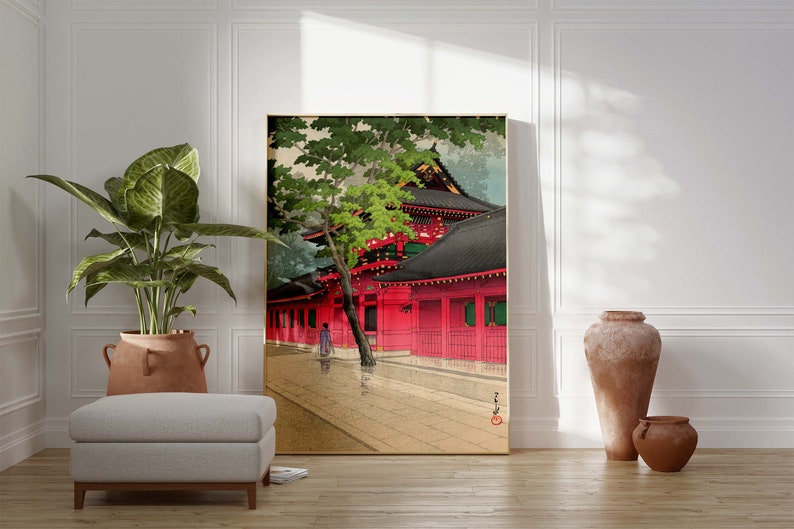 May include: A traditional Japanese woodblock print depicting a red temple with a green tree in the foreground. The temple has a black roof and is surrounded by a wooden fence. A person in a kimono is walking in the street.