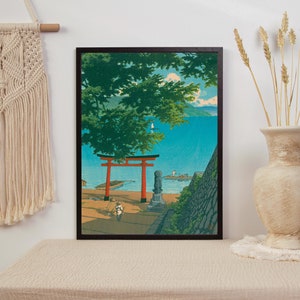 May include: A framed print of a Japanese landscape with a red torii gate, a stone statue, and a view of a blue body of water. The print is set against a white wall with a macrame wall hanging and a vase of dried wheat.
