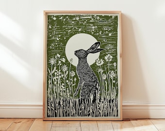 May include: A framed print featuring a black and white illustration of a hare in a field of flowers, with a full moon in the background. The artwork has a rustic, woodcut style, with a green and white color palette. The print is displayed on a wooden floor.