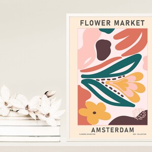 K&ouml;nnte beinhalten: Ein gerahmtes Poster mit einem abstrakten Blumenmuster in Rosa, Orange, Gelb, Gr&uuml;n und Braun. Das Poster zeigt den Text "FLOWER MARKET AMSTERDAM" und am unteren Rand den Text "FLOWERS EXHIBITION 2021 COLLECTION".