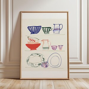 May include: A framed wall art print featuring a line drawing illustration of various kitchenware items arranged on three shelves. The artwork displays bowls, cups, and pitchers in blue, red, green, and pink colors against a light cream background.