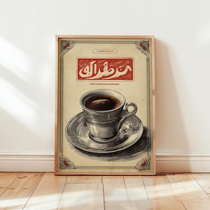 May include: A framed vintage-style print depicting a cup of coffee on a saucer. The cup and saucer are silver with detailed patterns. The print has a beige background with Arabic text in a red rectangle at the top.