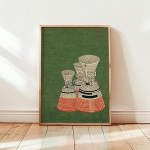 Peut inclure: Une affiche encadrée représentant trois illustrations stylisées de moteurs de fusée. Les moteurs sont de couleur crème et rouge avec des accents noirs, sur un fond vert. L'affiche est dans un cadre en bois, contre un mur blanc et un sol en bois.