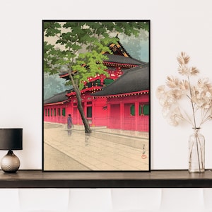 May include: A traditional Japanese woodblock print depicting a red temple with a green tree in the foreground. The temple has a black roof and white walls with red accents. A person in a purple robe walks in front of the temple.