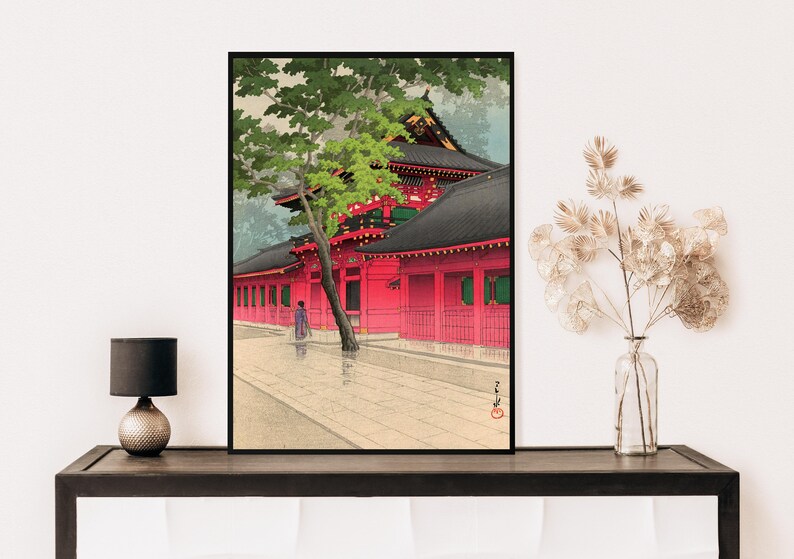 May include: A traditional Japanese woodblock print depicting a red temple with a green tree in the foreground. The temple has a black roof and white walls with red accents. A person in a purple robe walks in front of the temple.