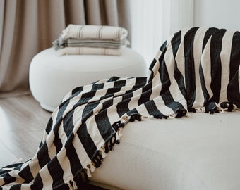 May include: A black and white striped throw blanket with fringe edges draped over a white couch. The blanket is made of a soft, textured fabric.