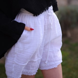 Puede incluir: Pantalones cortos blancos de tela texturizada y arrugada con cintura el&aacute;stica y cord&oacute;n blanco a juego. Los pantalones cortos tienen un corte relajado, bolsillos laterales y un dobladillo sin rematar y deshilachado en las perneras.