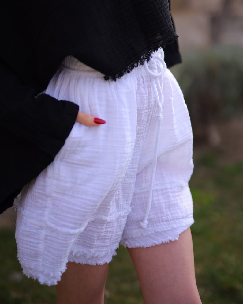 Puede incluir: Pantalones cortos blancos de tela texturizada y arrugada con cintura el&aacute;stica y cord&oacute;n blanco a juego. Los pantalones cortos tienen un corte relajado, bolsillos laterales y un dobladillo sin rematar y deshilachado en las perneras.