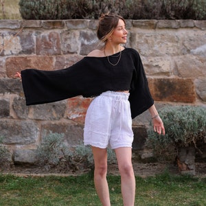May include: A woman wearing a black, cropped, off-the-shoulder top with white, ruffled shorts and white sneakers.