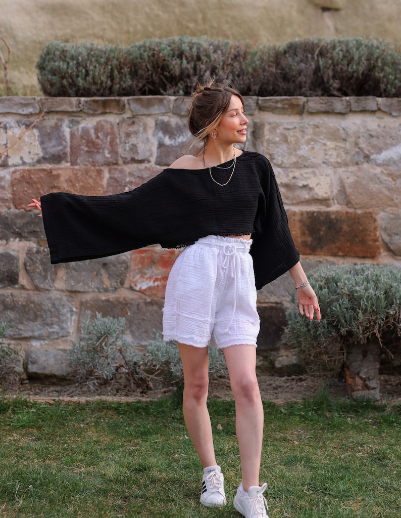 Puede incluir: Un top corto negro de manga larga con mangas anchas y dobladillo sin rematar, combinado con pantalones cortos blancos de talle alto con cintura el&aacute;stica con cord&oacute;n y dobladillo sin rematar. El conjunto se completa con zapatillas blancas.