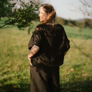 May include: A black short-sleeved top with a wide, loose fit and a round neckline, paired with matching black trousers that feature side pockets. The set is constructed from a solid-colored fabric with a visible texture, worn as a coordinated outfit.