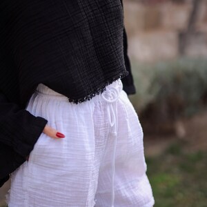 May include: White cotton shorts with a drawstring waist and frayed edges. The shorts are worn with a black off-the-shoulder top.