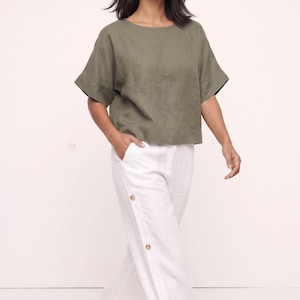 May include: An olive green short-sleeved top with a round neckline paired with white wide-leg trousers featuring a vertical row of three visible brown buttons along the side seam and side pockets, creating a coordinated two-piece outfit.