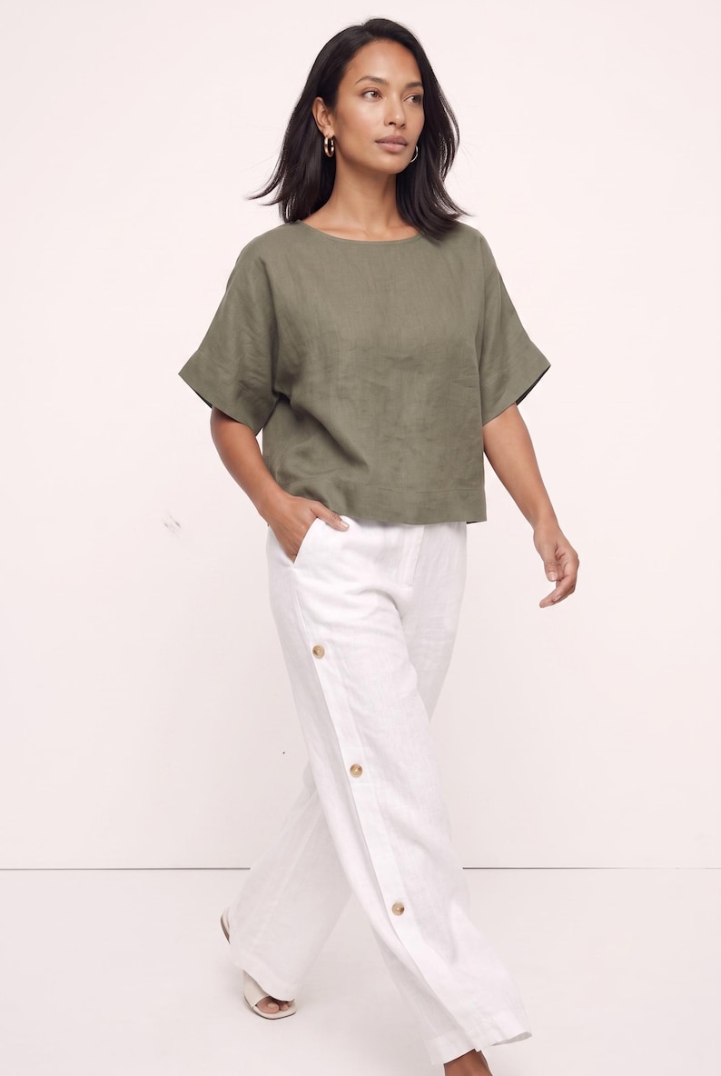 May include: An olive green short-sleeved top with a round neckline paired with white wide-leg trousers featuring a vertical row of three visible brown buttons along the side seam and side pockets, creating a coordinated two-piece outfit.