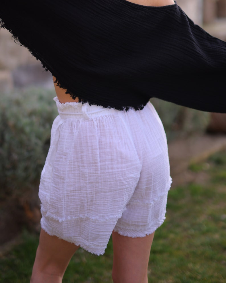 Puede incluir: Pantalones cortos blancos con cintura alta el&aacute;stica y fruncida, confeccionados en un tejido texturizado y arrugado. Los pantalones cortos tienen un corte holgado con bordes deshilachados en el dobladillo y costuras horizontales en las piernas.