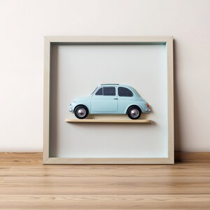 Può includere: Un'auto giocattolo azzurra con ruote nere e tetto nero è esposta su una piccola mensola di legno all'interno di una cornice quadrata. La cornice è di colore chiaro e lo sfondo è azzurro chiaro. L'auto ha un design classico.