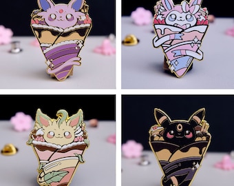 May include: Four enamel pins featuring Pokemon characters in a crepe. The pins are gold, purple, pink, and black. Each pin features a different Pokemon character.