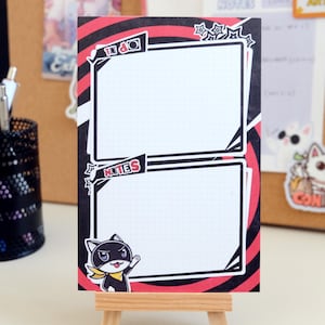 May include: A black and red patterned notepad with two sections labeled "To Do" and "Notes". The notepad features a cartoon black cat with a yellow collar and a red mask.