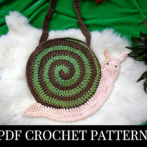 May include: Crochet pattern for a snail-shaped bag. The bag is made of green, brown, and pink yarn and has a spiral shell design. The pattern is available as a PDF download.
