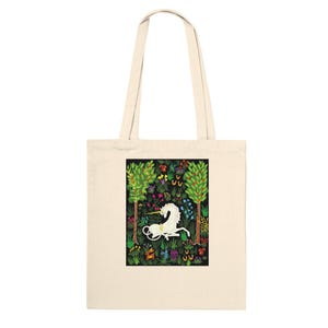 May include: Cream-coloured tote bag with a black rectangular design featuring a white unicorn in a garden. The garden has green trees, colourful flowers, and butterflies. The bag has two cream-coloured handles.