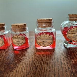 May include: Four glass bottles filled with red liquid and cork stoppers. Each bottle has a label with the text "Healing Potion", "Greater Healing Potion", "Superior Healing Potion", and "Supreme Healing Potion". The labels also include the text "Marigold Tavern" and a number.