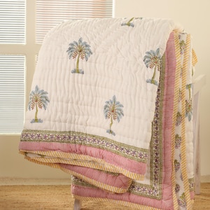 May include: White cotton quilt with a hand-block printed design of palm trees. The quilt has a pink and yellow striped border with a green floral pattern.