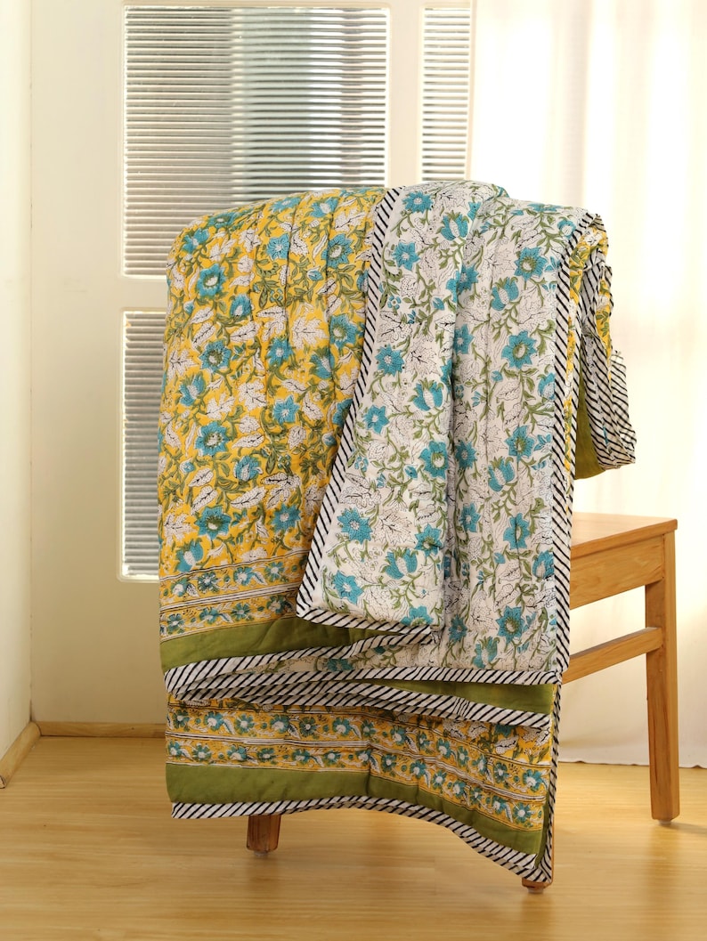 Puede incluir: Un edred&oacute;n con estampado floral sobre una silla de madera. El edred&oacute;n presenta un fondo amarillo con flores azules y blancas. El borde es verde con rayas blancas y negras. El edred&oacute;n est&aacute; hecho de un material suave y c&oacute;modo.