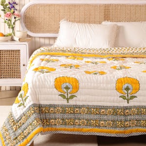 May include: White cotton quilt with a yellow floral print. The quilt has a border with a green and yellow floral pattern. The quilt is on a bed with a white headboard.