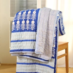 May include: A blue and white patterned quilt draped over a wooden chair. The quilt features floral and striped designs, with a blue border. The quilt is made of soft, quilted fabric, perfect for adding a touch of comfort and style to any room.