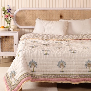 May include: White cotton quilt with a palm tree print and a yellow, pink, and green border. The quilt is on a bed with a white headboard and a white wicker headboard.