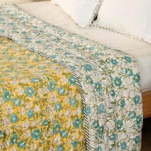 Puede incluir: Un edred&oacute;n con estampado floral en tonos amarillos, turquesa y blanco. El edred&oacute;n presenta un patr&oacute;n repetido de flores y hojas. El borde es una raya en blanco y negro. El edred&oacute;n est&aacute; sobre una cama con almohadas blancas.