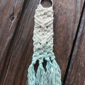 May include: A white and light blue macrame keychain with a silver key ring and long tassels.