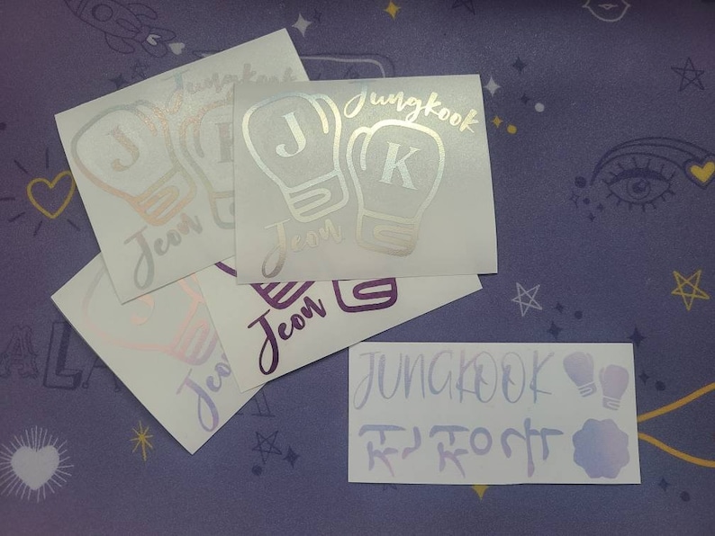 K&ouml;nnte beinhalten: Vier wei&szlig;e Vinyl-Aufkleber mit einem Boxhandschuh-Design. Die Handschuhe sind silbern umrandet und haben einen Buchstaben J oder K im Inneren. Die Aufkleber sagen "Jungkook" und "Jeon" in einer silbernen Schrift.