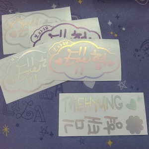 K&ouml;nnte beinhalten: Vier schimmernde Aufkleber mit koreanischem Text. Die Aufkleber haben die Form von Wolken und zeigen ein Herzdesign. Der Text auf den Aufklebern lautet "taehyung" und "ich liebe dich".